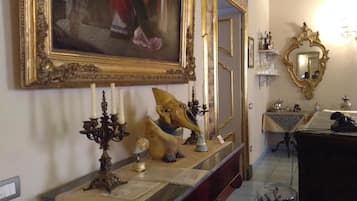 A room with a large ornate mirror, a framed painting, a candelabra, and a decorative vase on a console table.