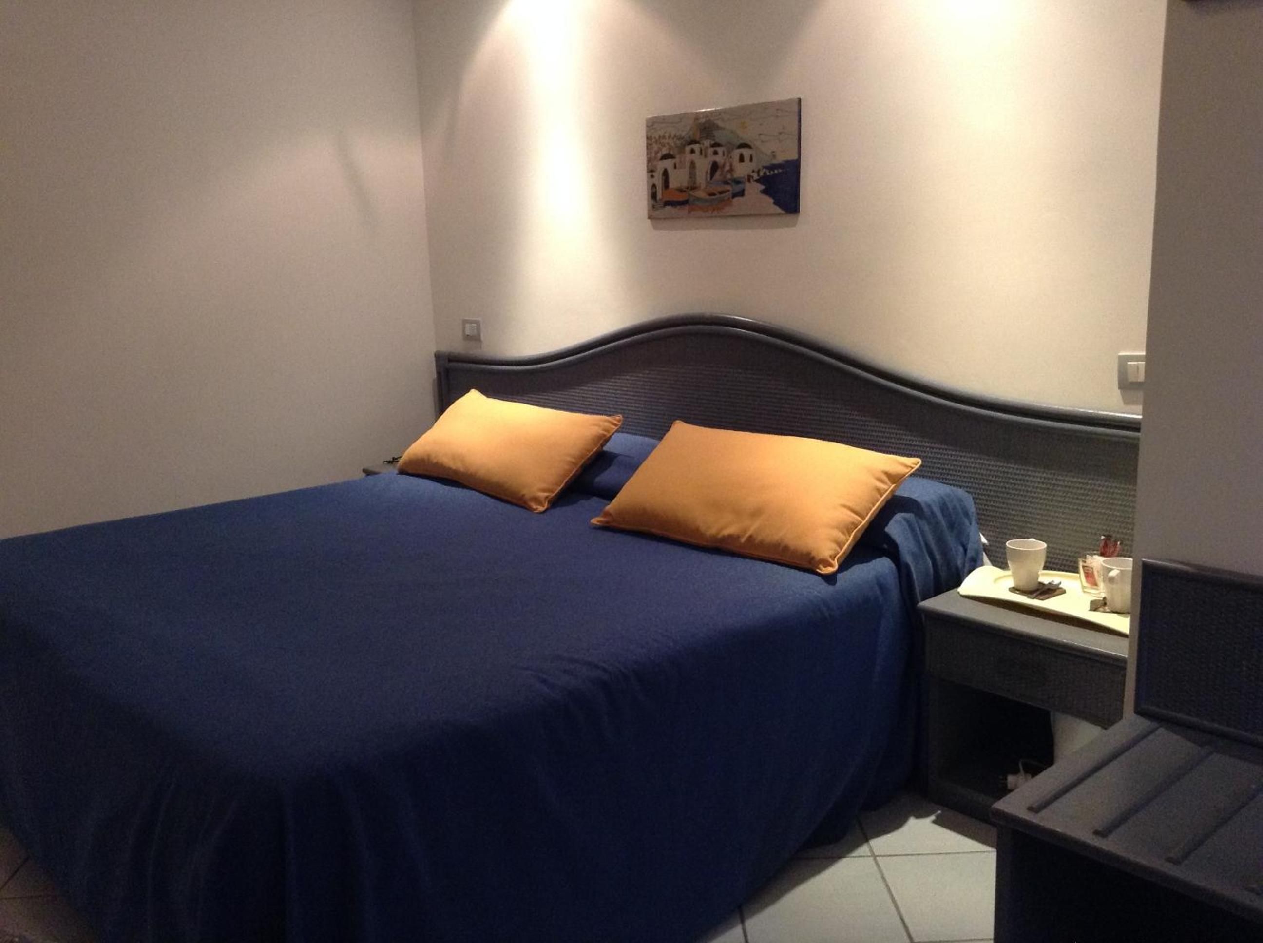 Ein Zimmer mit einem Bett, zwei Kissen, einem Nachttisch und einem Bild an der Wand.