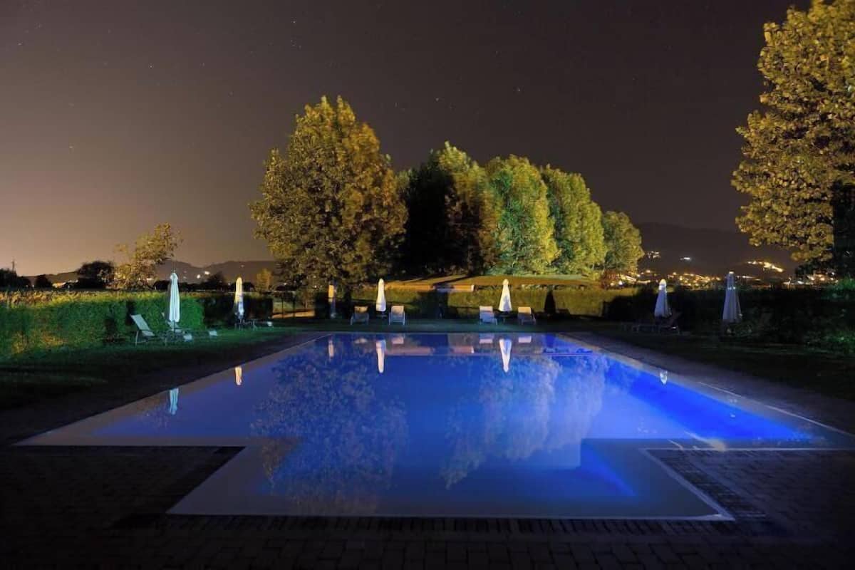 A rectangular pool with a clear water surface, surrounded by trees and a paved walkway.