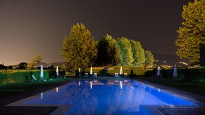 A nighttime swimming pool with a clear reflection, surrounded by trees and lounge chairs. - Hotel Le Capanne (Arezzo)