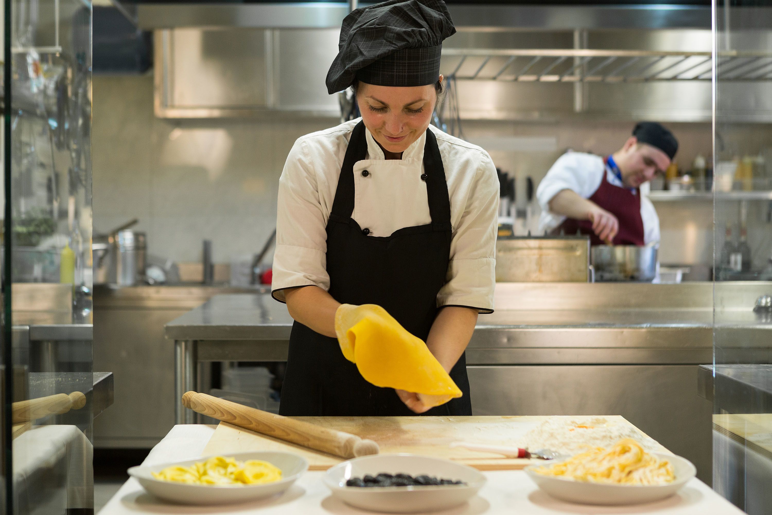 Uno chef prepara il cibo in una cucina professionale, dotata di elettrodomestici in acciaio inossidabile e un ambiente di lavoro pulito e ordinato.