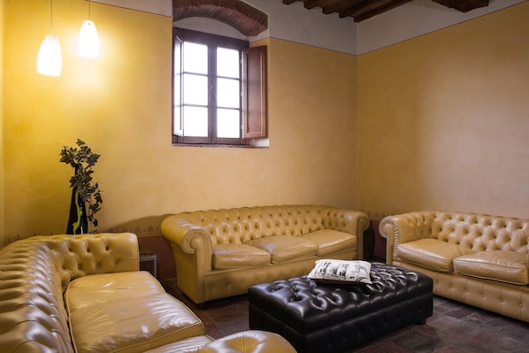A living room with a beige sofa set, a black ottoman, and a potted plant. - Hotel Le Capanne (Arezzo)