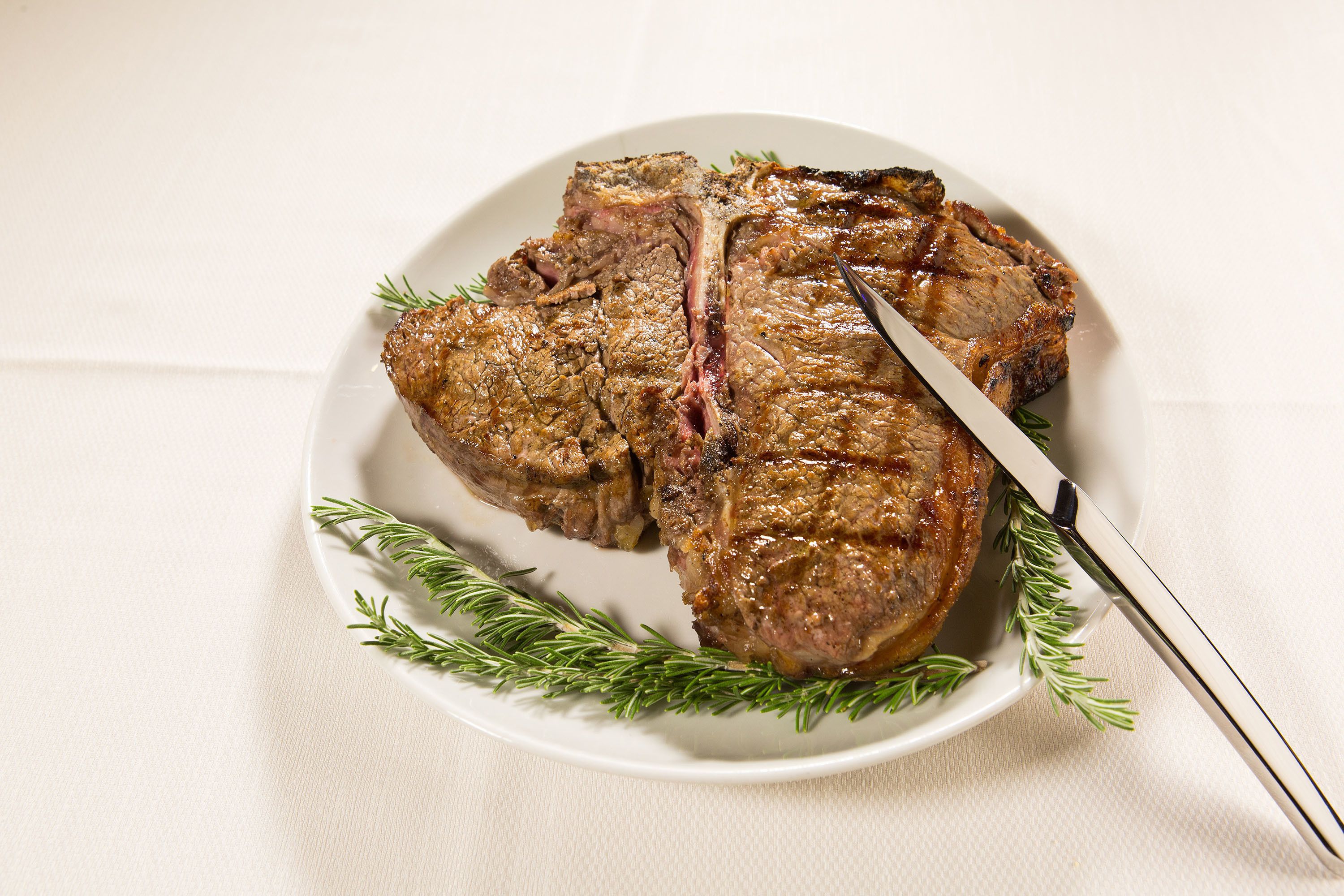 A plate of steak with a knife and rosemary garnish.