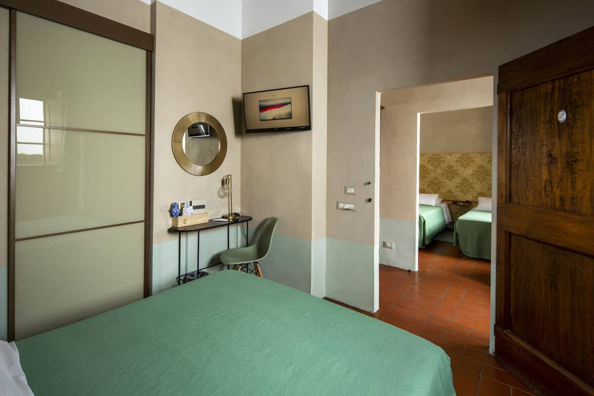 A hotel room with a bed, a desk with a chair, a mirror, and a television.