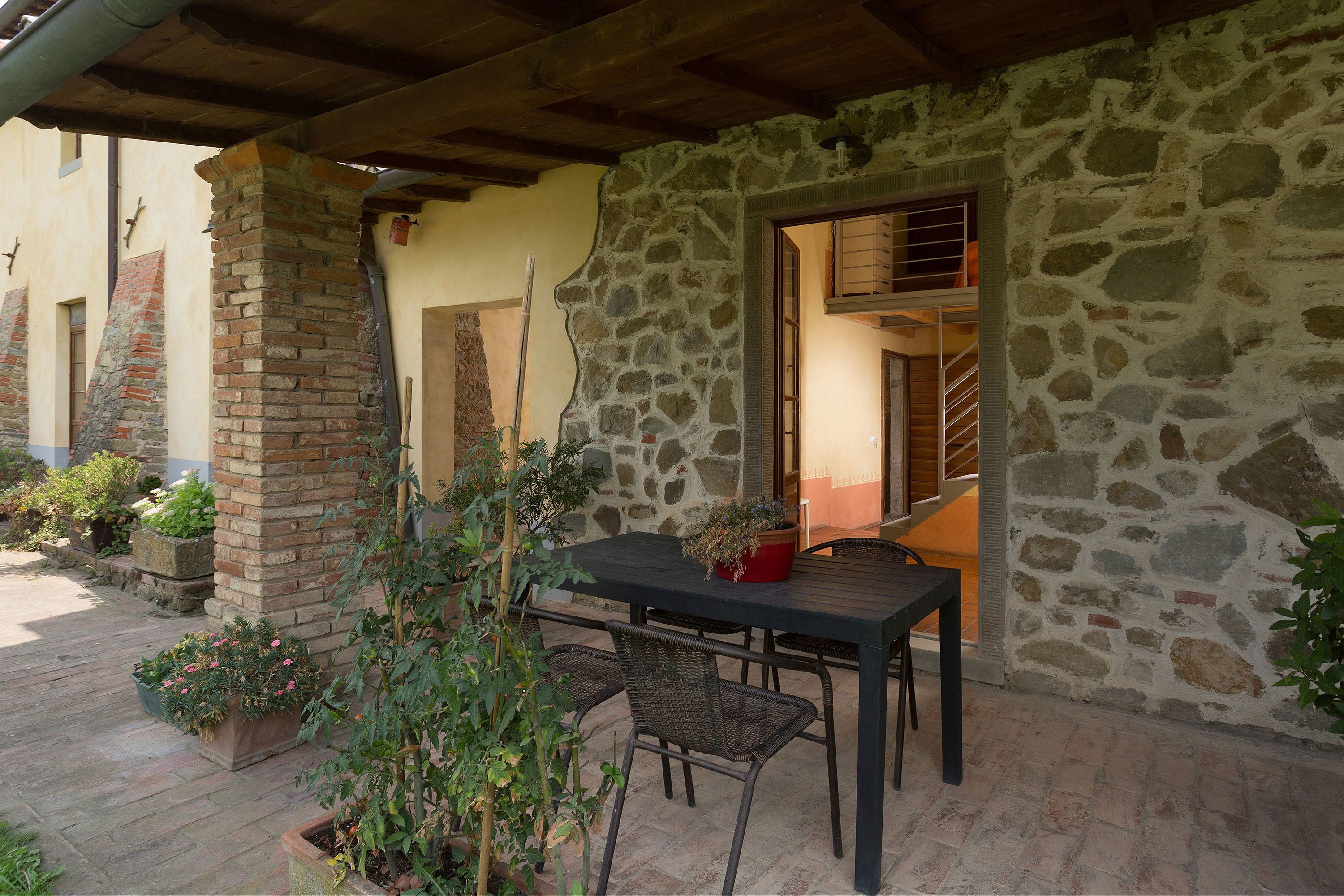 An outdoor patio with a stone wall, a wooden table, and wicker chairs.