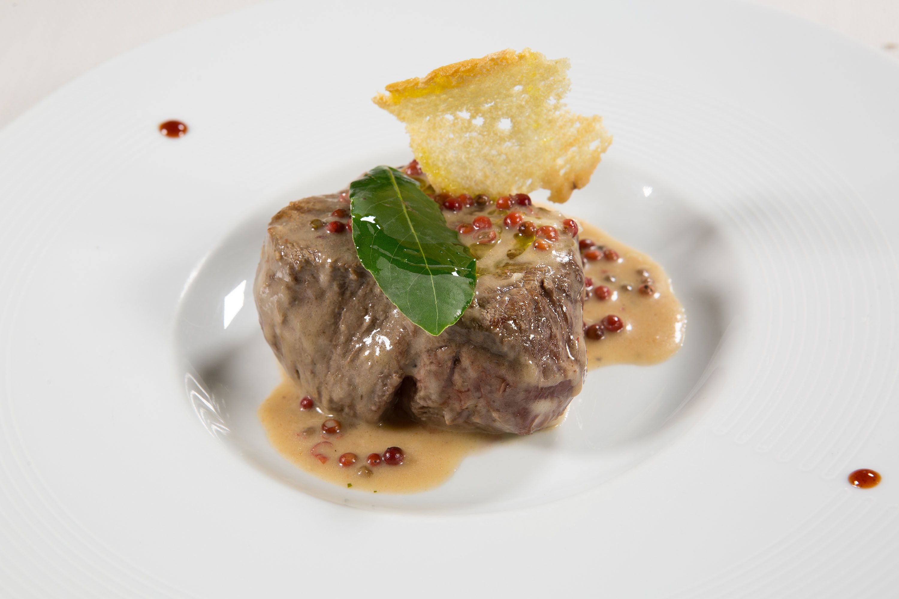 A plate with a meat dish, sauce, and a garnish.