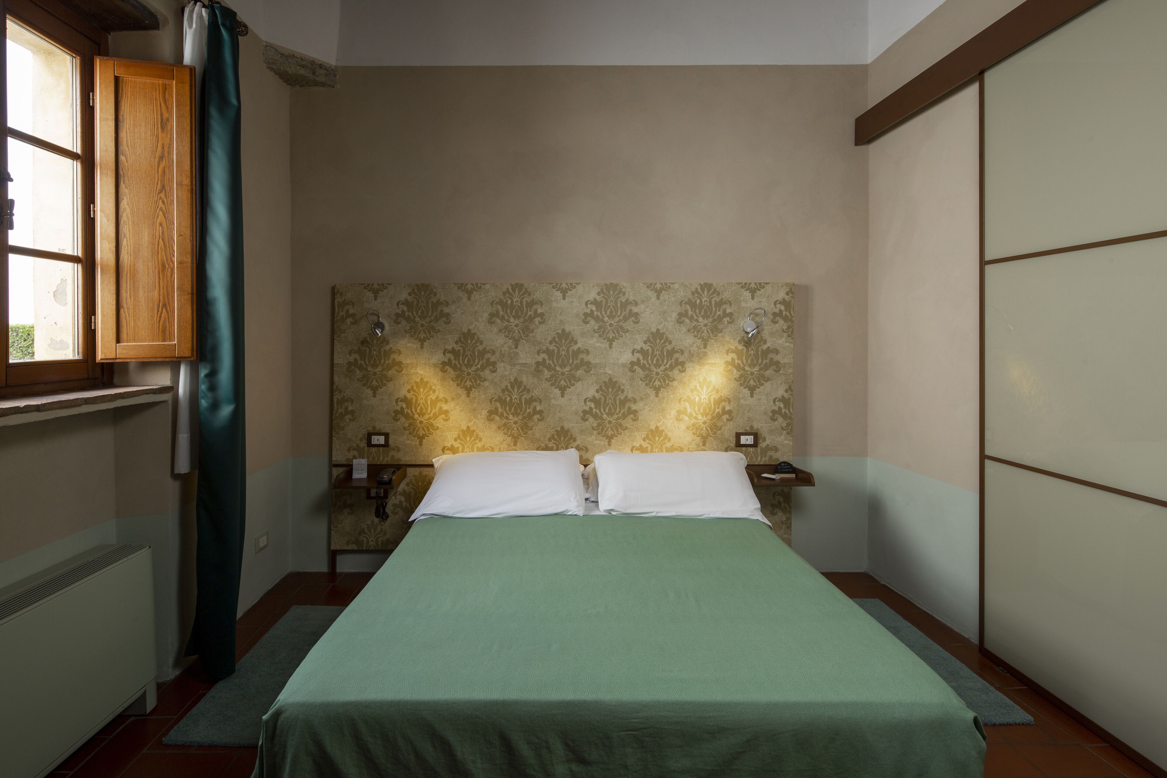 A bedroom with a bed, a nightstand, a window with curtains, and a wall with a patterned design.