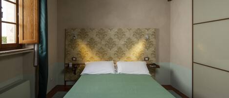 A bedroom with a bed, a nightstand, a window with curtains, and a wall with a patterned design.
