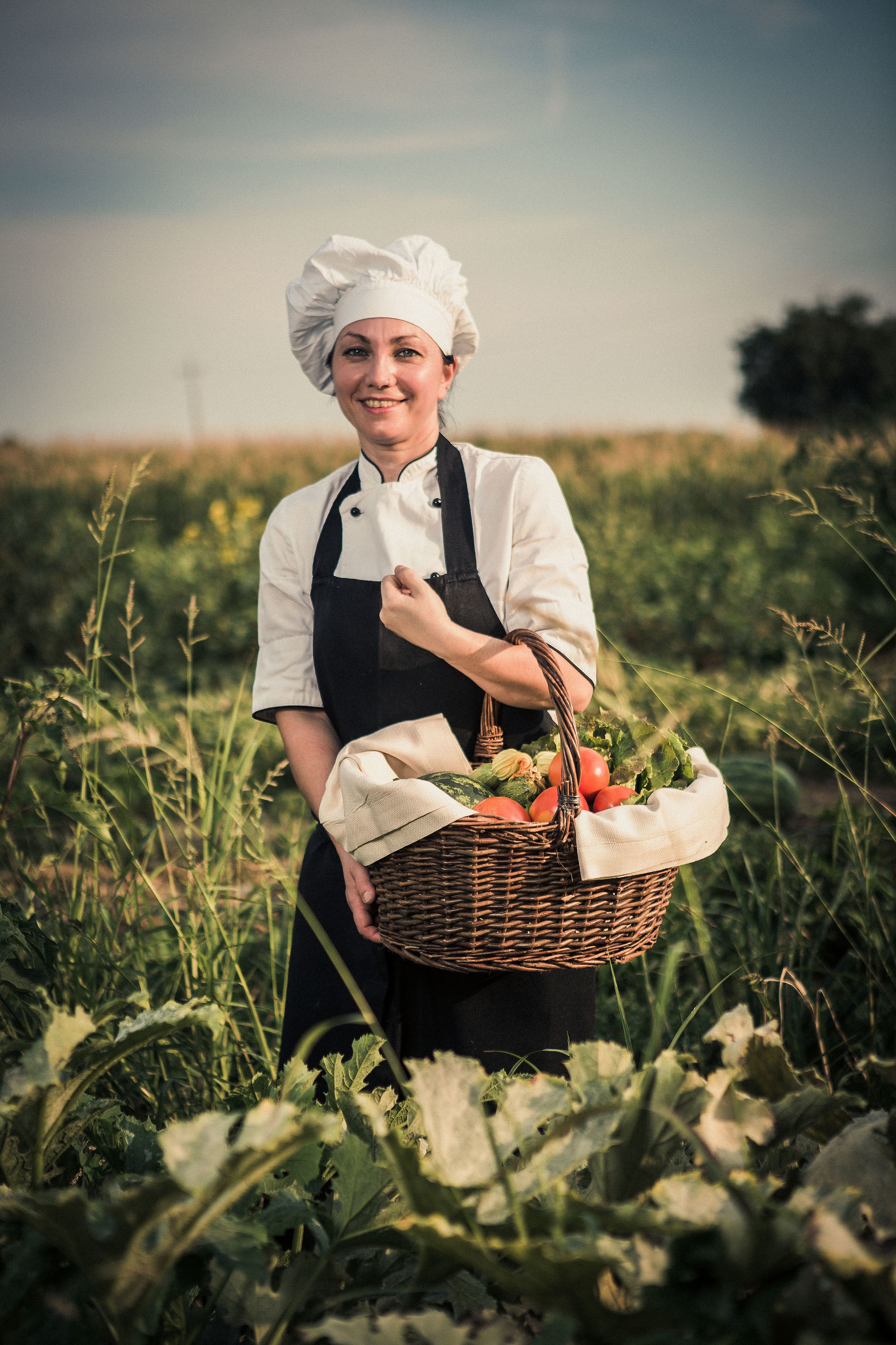 A chef in a field holding a basket of vegetables.