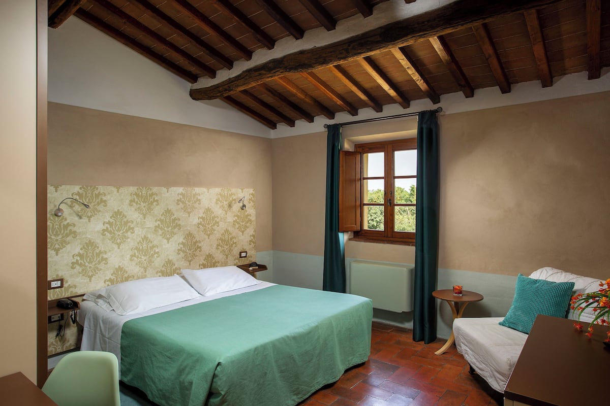 A bedroom with a bed, a chair, a small table, and a window with curtains.