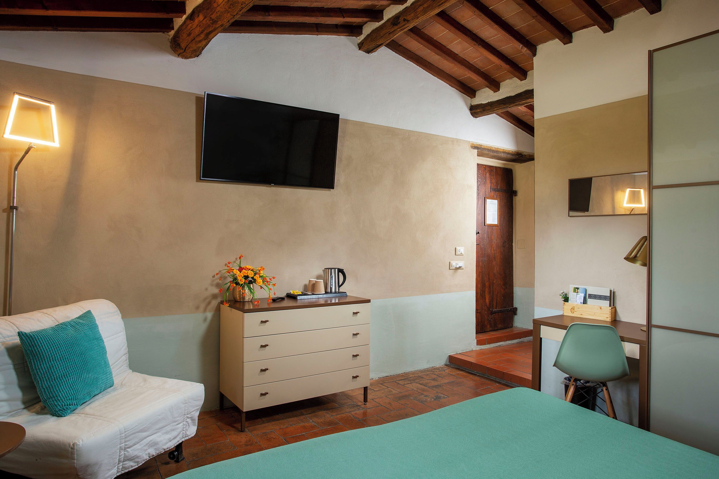 Un dormitorio con cama, cómoda, escritorio con silla, televisor y lámpara.