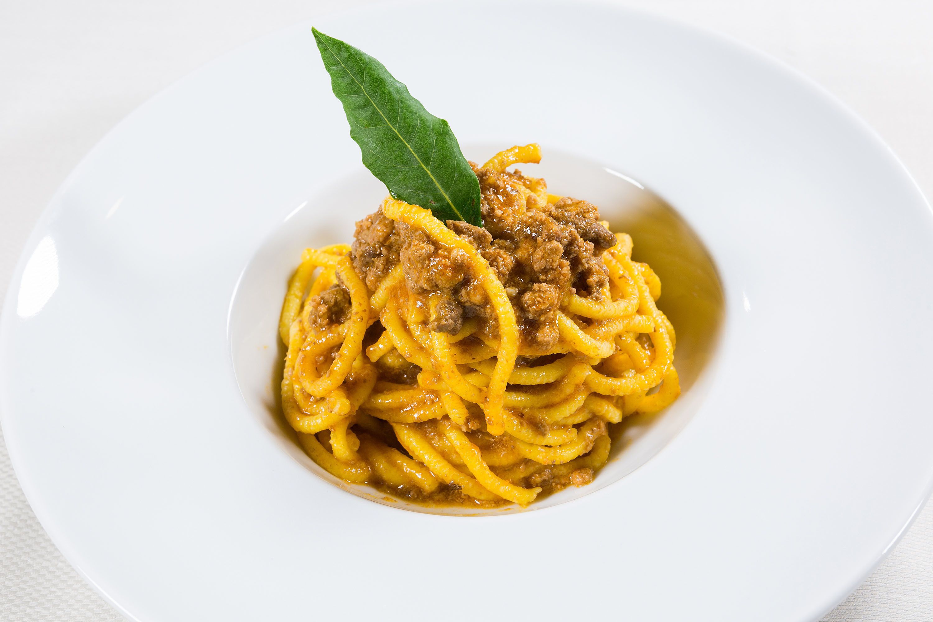Un piatto di spaghetti con ragù e una foglia di alloro come guarnizione.