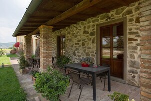 Un edificio de piedra con un patio cubierto, mesas al aire libre y plantas en macetas.