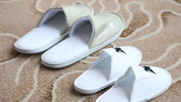 A pair of white slippers with a black logo on a patterned carpet.