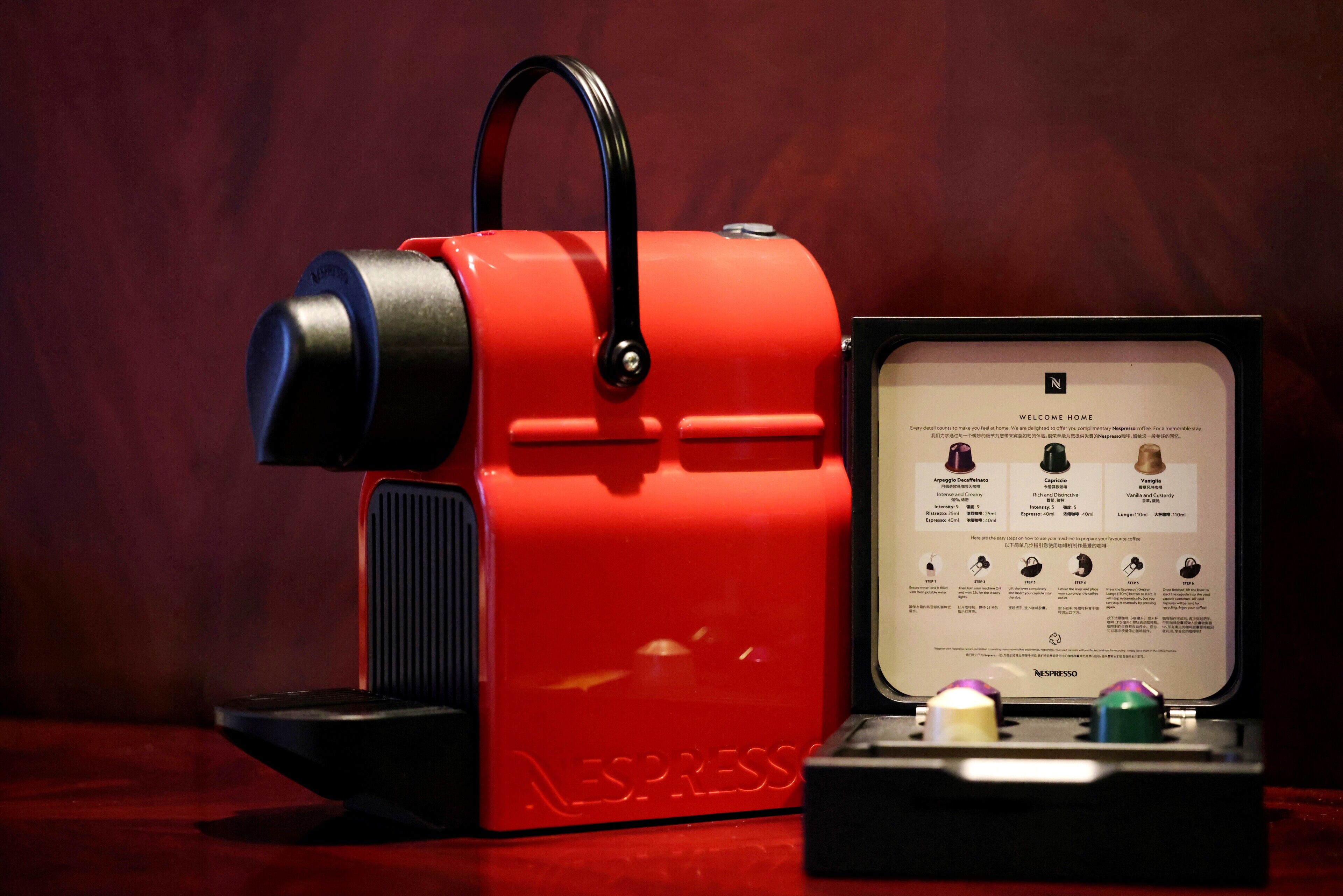 Una cafetera roja Nespresso con manual de instrucciones y un portacapsulas de café.