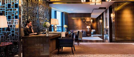 A modern hotel lobby with a reception desk, seating area, and decorative wall panels.