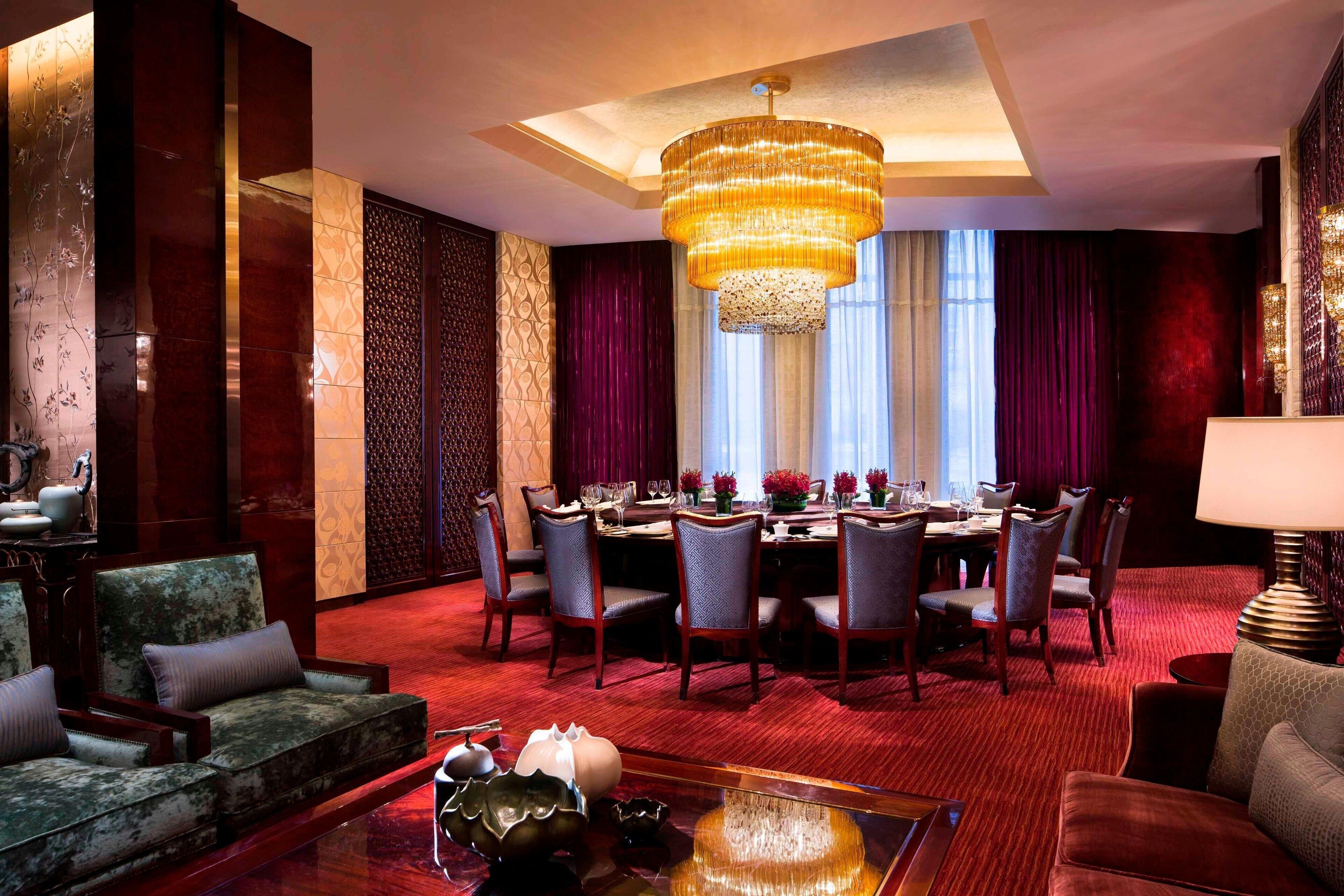 A hotel room with a round dining table, multiple chairs, a chandelier, and a red carpeted floor.