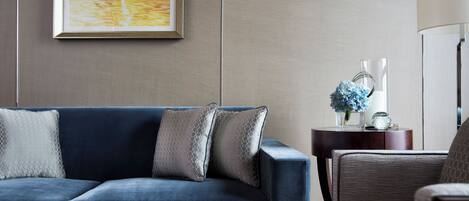 A modern living room with a blue sofa, two decorative pillows, a side table with a vase of flowers, and a lamp.