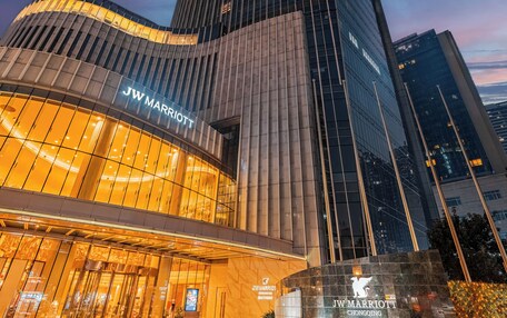 A JW Marriott hotel with a modern glass facade, a curved entrance, and a well-lit plaza area.