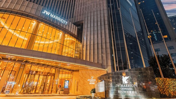 Un hotel JW Marriott con fachada de vidrio moderna, una entrada curva y un área de plaza bien iluminada.