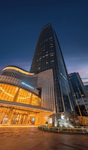 Un hôtel JW Marriott doté d’une façade moderne en verre, d’une entrée incurvée et d’une place bien éclairée.