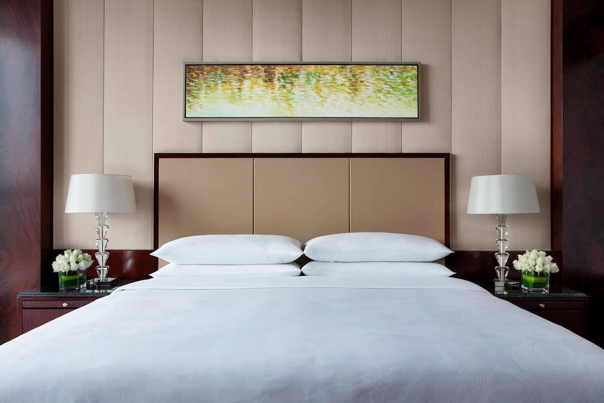 Ein Hotelzimmer mit einem großen Bett, zwei Nachttischen mit Lampen, einem gerahmten Kunstwerk über dem Bett und einem Holzkopfstück.