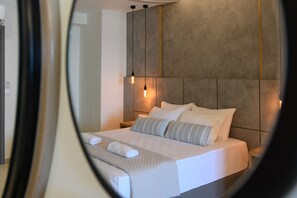A neatly made bed with white linens and a grey quilt, a headboard with a light fixture, and a small bedside table with a lamp.