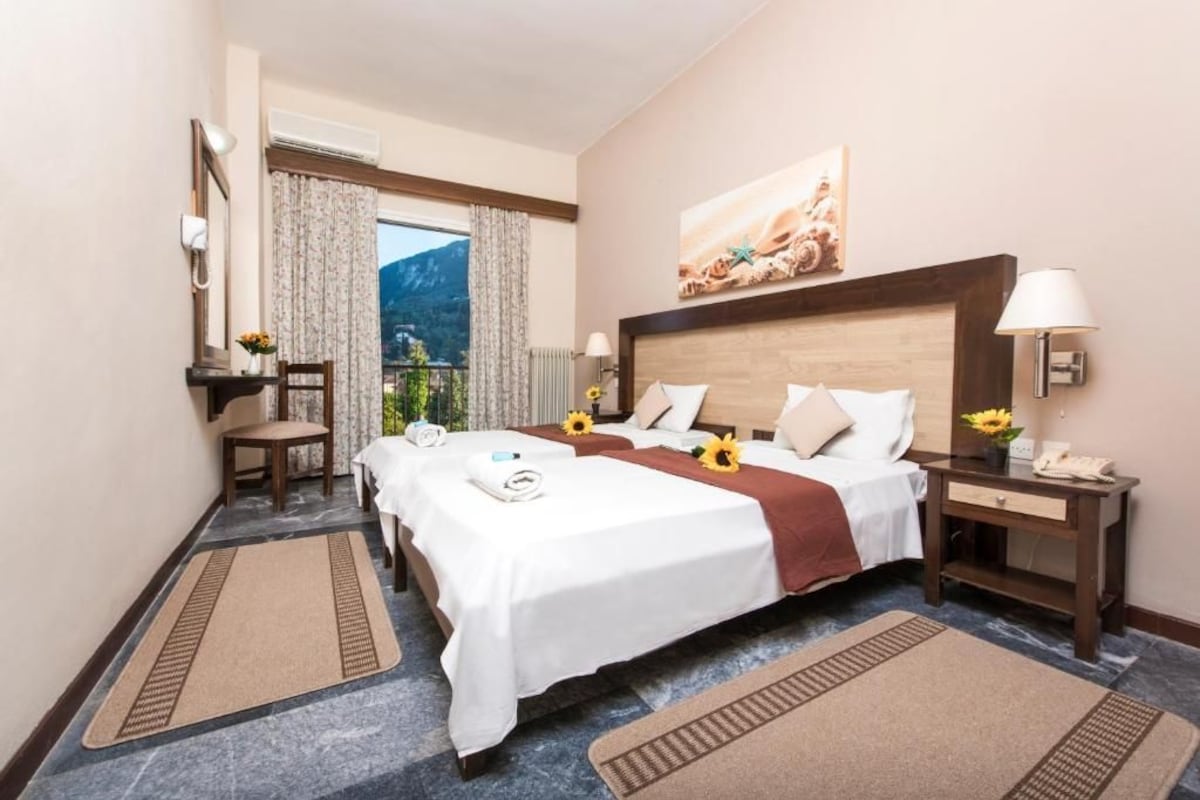 Habitación de hotel con dos camas, un escritorio, una silla, una ventana con cortinas y un cuadro en la pared.