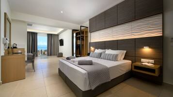 A modern hotel room with a large bed, a desk, and a view of the sea.