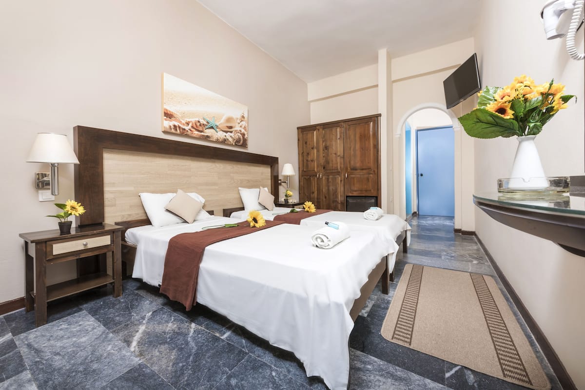 A hotel room with two beds, a wooden headboard, a painting, a TV, a wardrobe, and a bathroom with a mirror and sink.