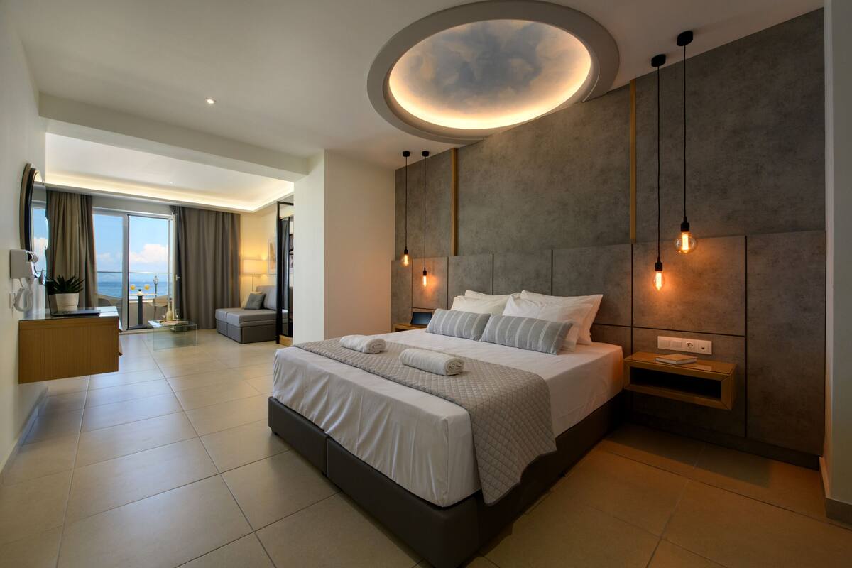 A modern bedroom with a large bed, a built-in desk, and a view of the sea.