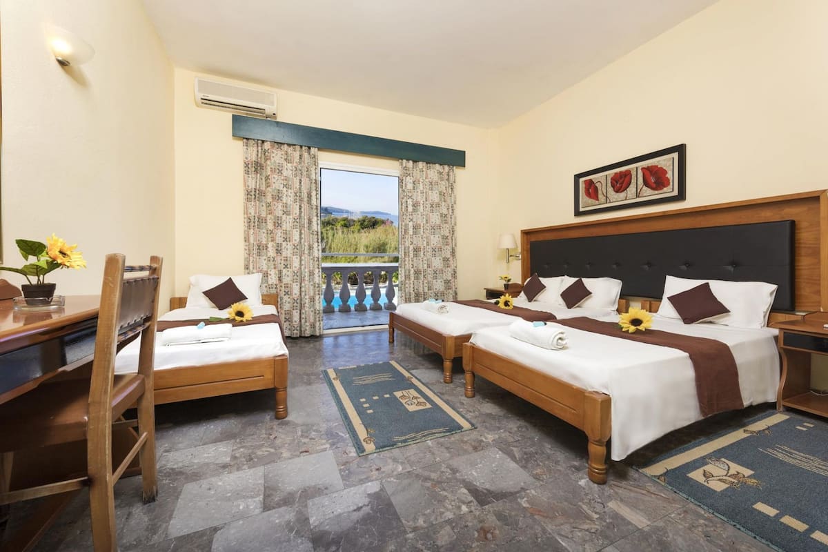 A hotel room with two beds, a desk, and a chair. There is a view of a pool and greenery outside.