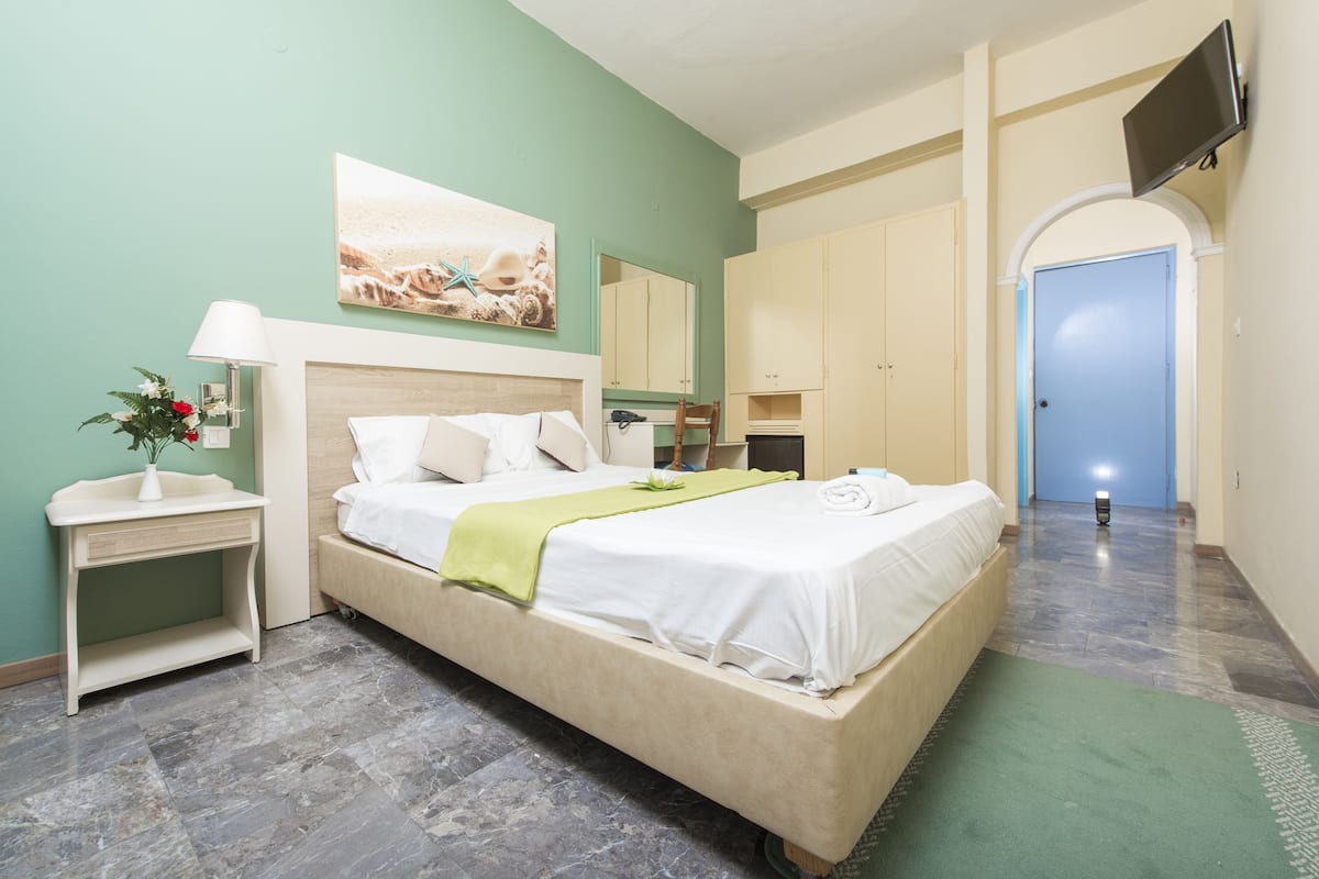 A hotel room with a bed, a nightstand, a lamp, a mirror, and a TV mounted on the wall.