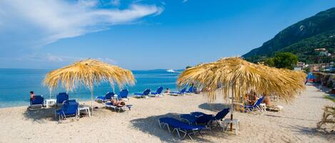 A beach with blue lounge chairs and straw umbrellas.