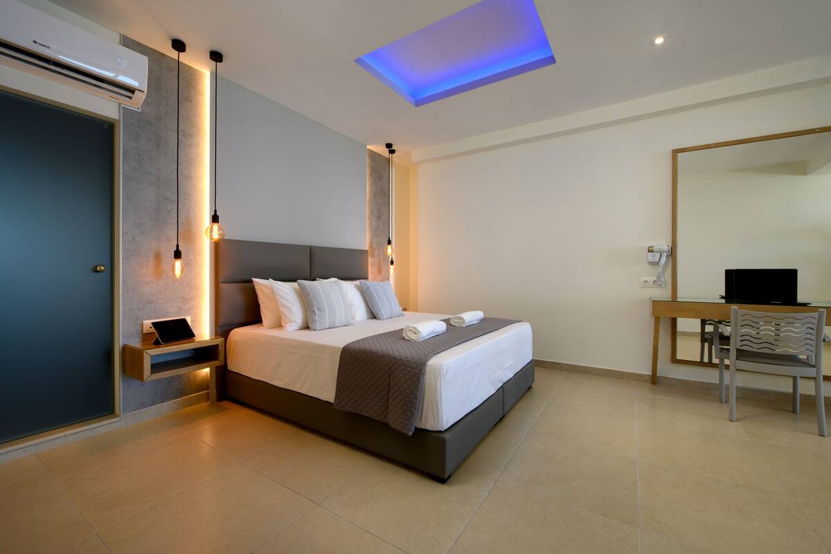 A modern hotel room with a large bed, bedside tables, a desk, and a flat-screen TV.