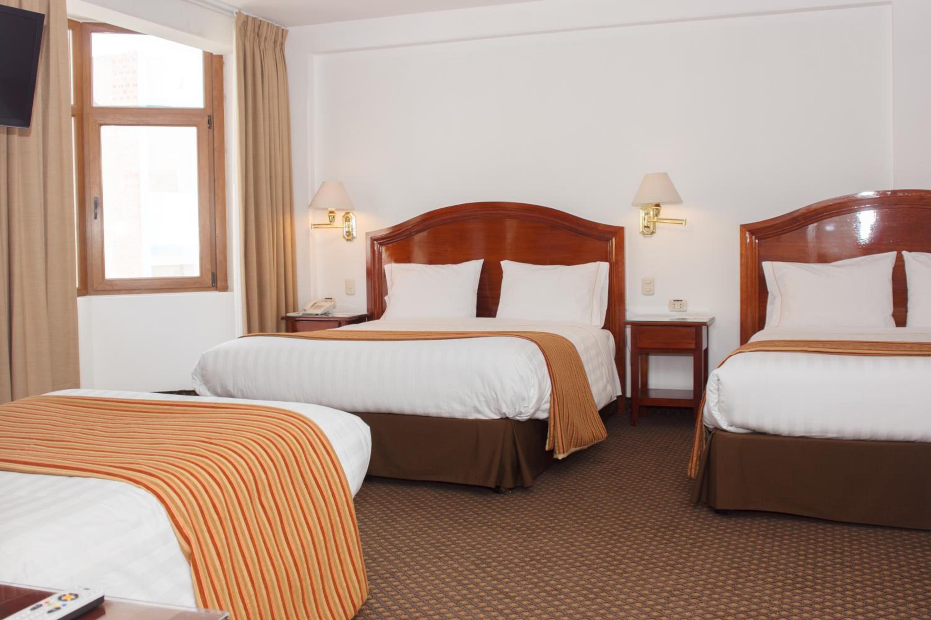 Une chambre d’hôtel avec deux lits simples, une petite table de chevet avec une lampe, une fenêtre avec des rideaux et un sol recouvert de moquette.