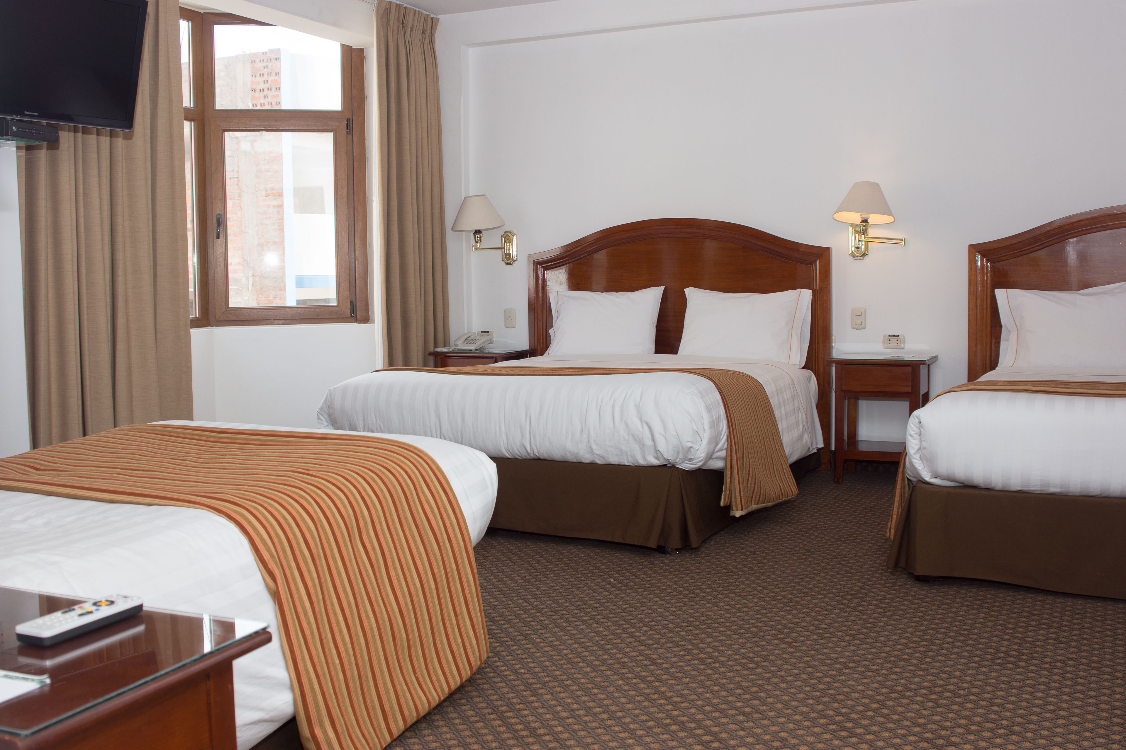 A hotel room with two beds, a TV, a desk, and a window with curtains.