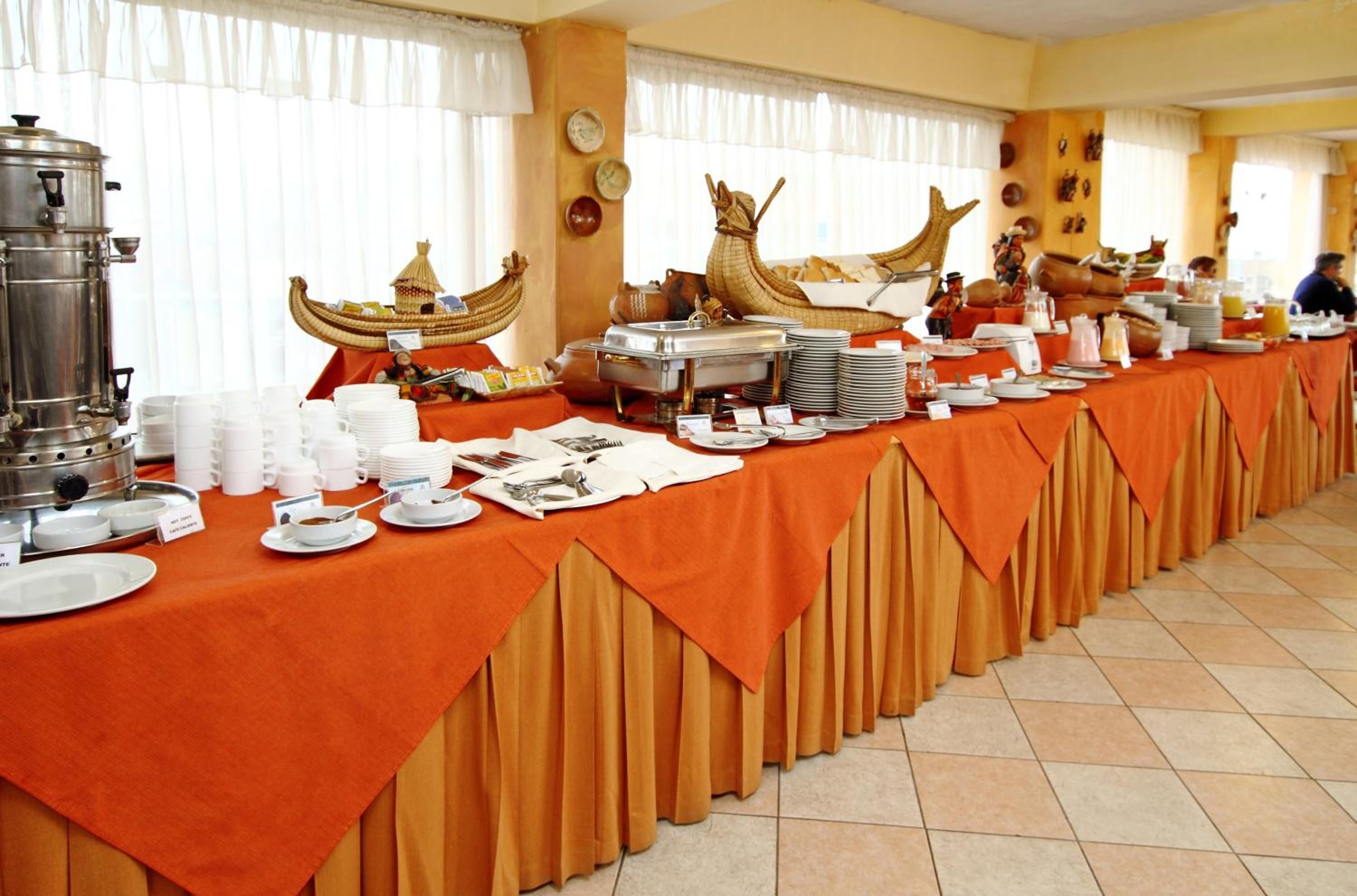 A buffet setup with a long table covered in an orange tablecloth, various food items, and a coffee station.