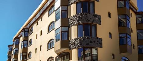 Un hotel de varios pisos con balcones, una entrada a nivel de calle y un cielo despejado.