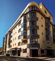 Un hotel de varios pisos con balcones, una entrada a nivel de calle y un cielo despejado.