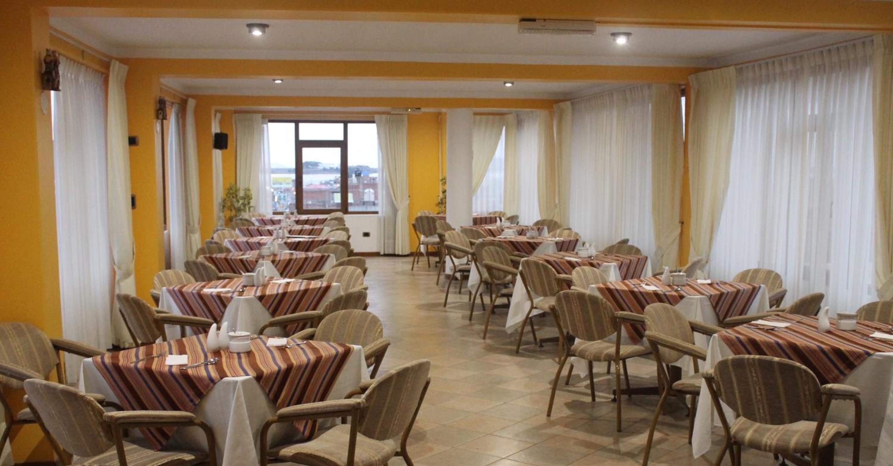 Un comedor con varias mesas y sillas, ventanas amplias con cortinas, y vista al exterior.