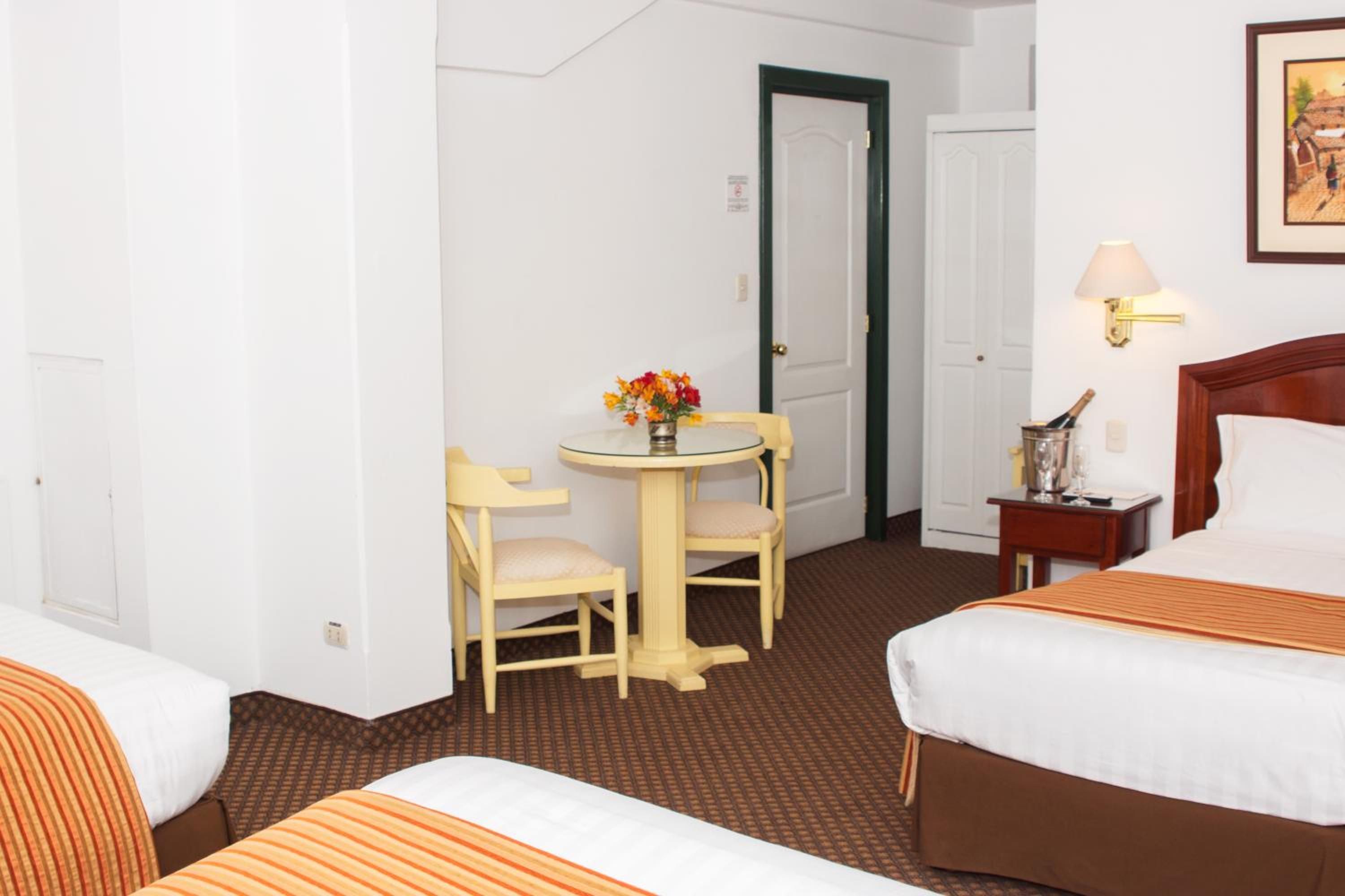 Une chambre d’hôtel avec deux lits, une petite table avec une chaise, une lampe et un tableau au mur.