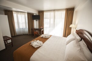 Una habitación de hotel con cama, escritorio, silla, televisor y lámpara.