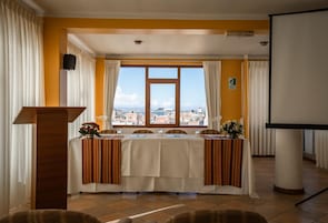 Un salón de conferencias con una mesa dispuesta para una reunión, un atril y un amplio ventanal con vistas a la ciudad.