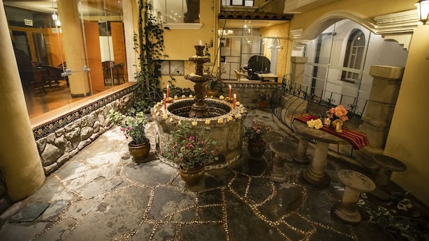 A courtyard with a central fountain, stone flooring, potted plants, and a table with flowers. - Hacienda Puno (Puno)