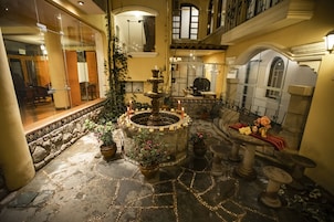 Un patio con una fuente central, suelo de piedra, plantas en macetas y una mesa con flores.