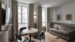 A modern living room with a round table, two chairs, a sofa, and a TV mounted on the wall. - Base Lausanne (Lausanne)