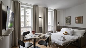 A hotel room with a bed, a desk with a chair, a round table with a chair, and a TV on the wall. - Base Lausanne (Lausanne)