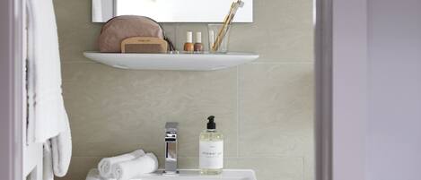 Een badkamer met een witte wastafel, een spiegel en een plank met toiletartikelen.