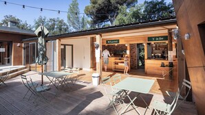 Een terras buiten met tafels, stoelen, een pizzaoven en een bar.